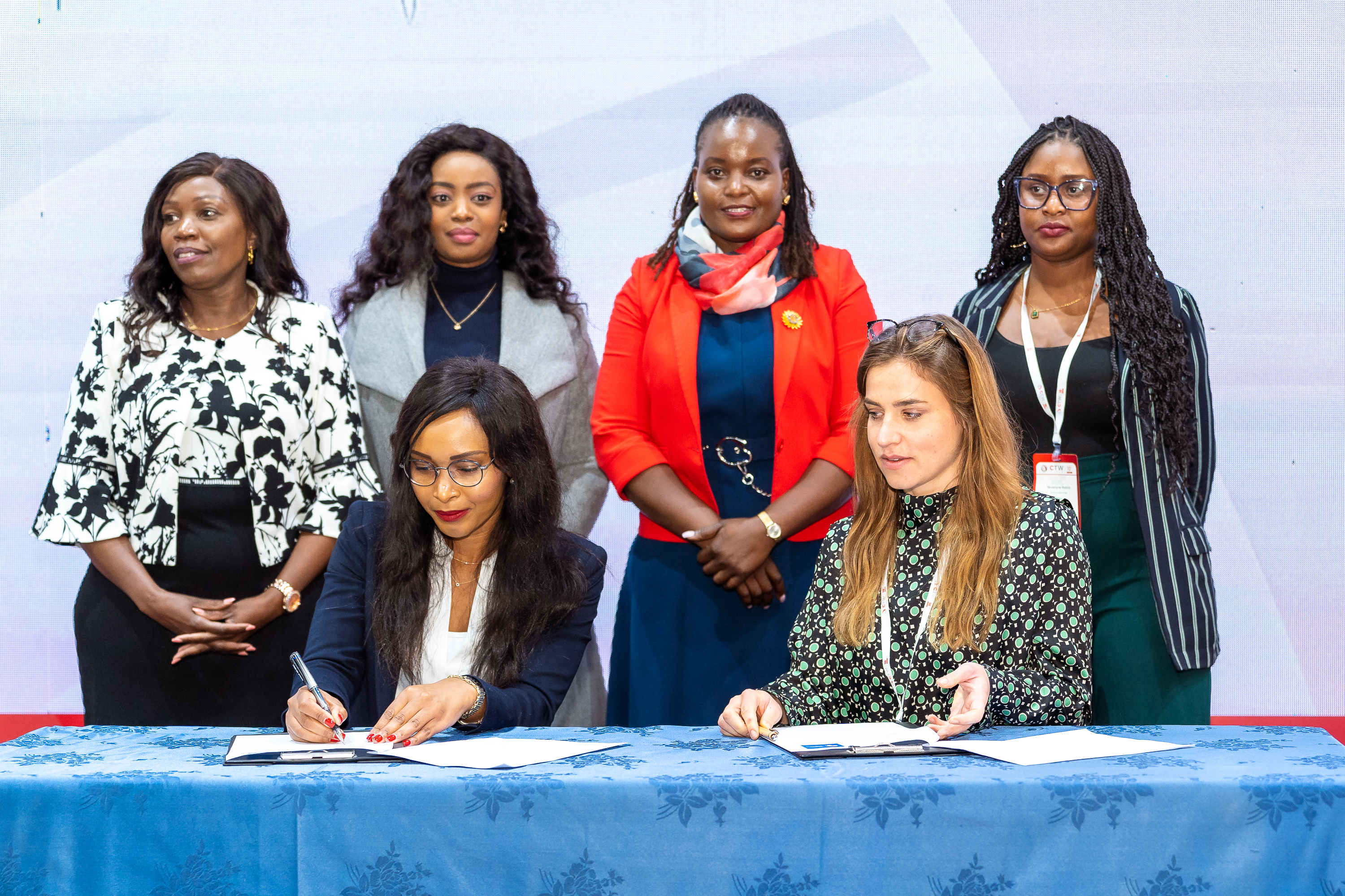 Two women signing an agreement as others look on