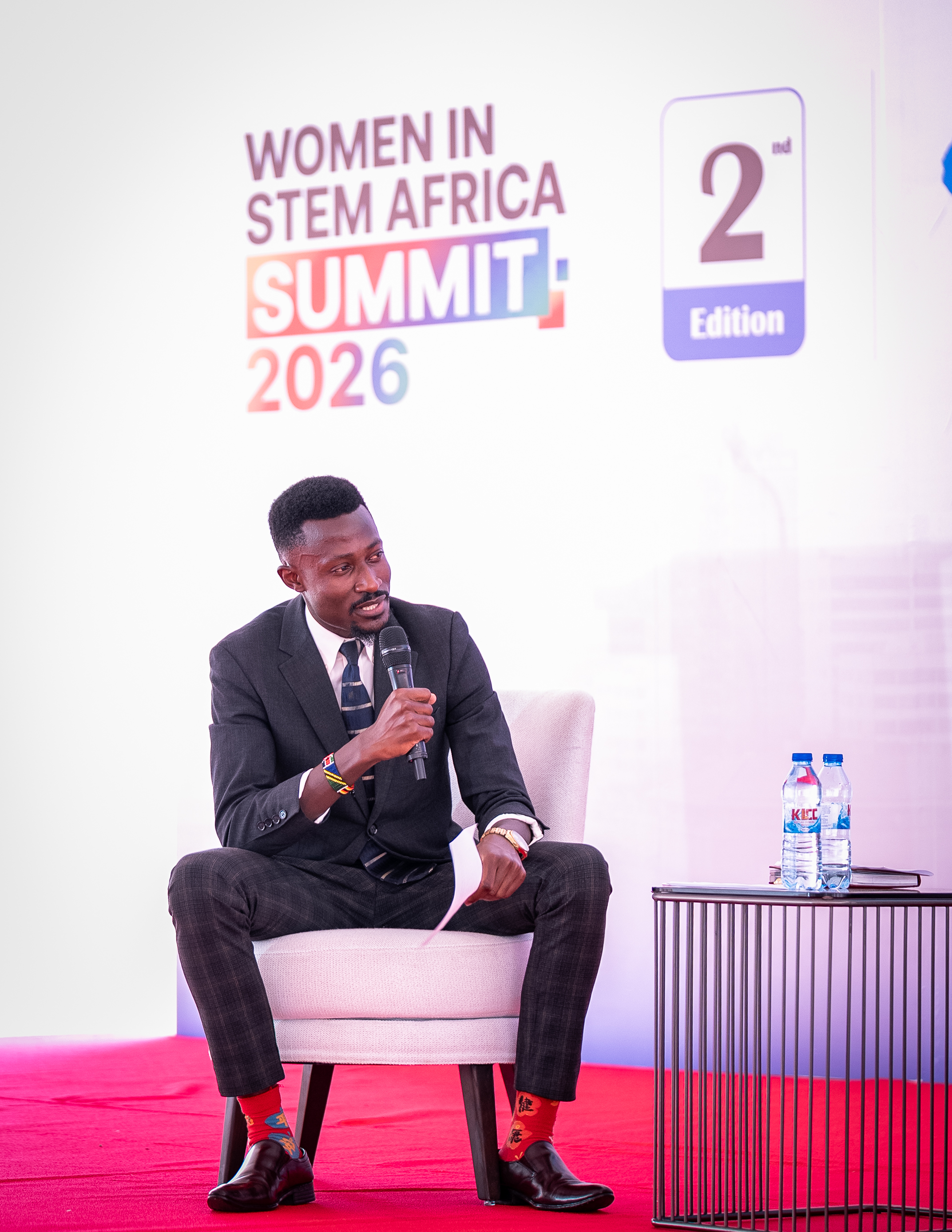 A speaker seated on stage, speaking into a microphone