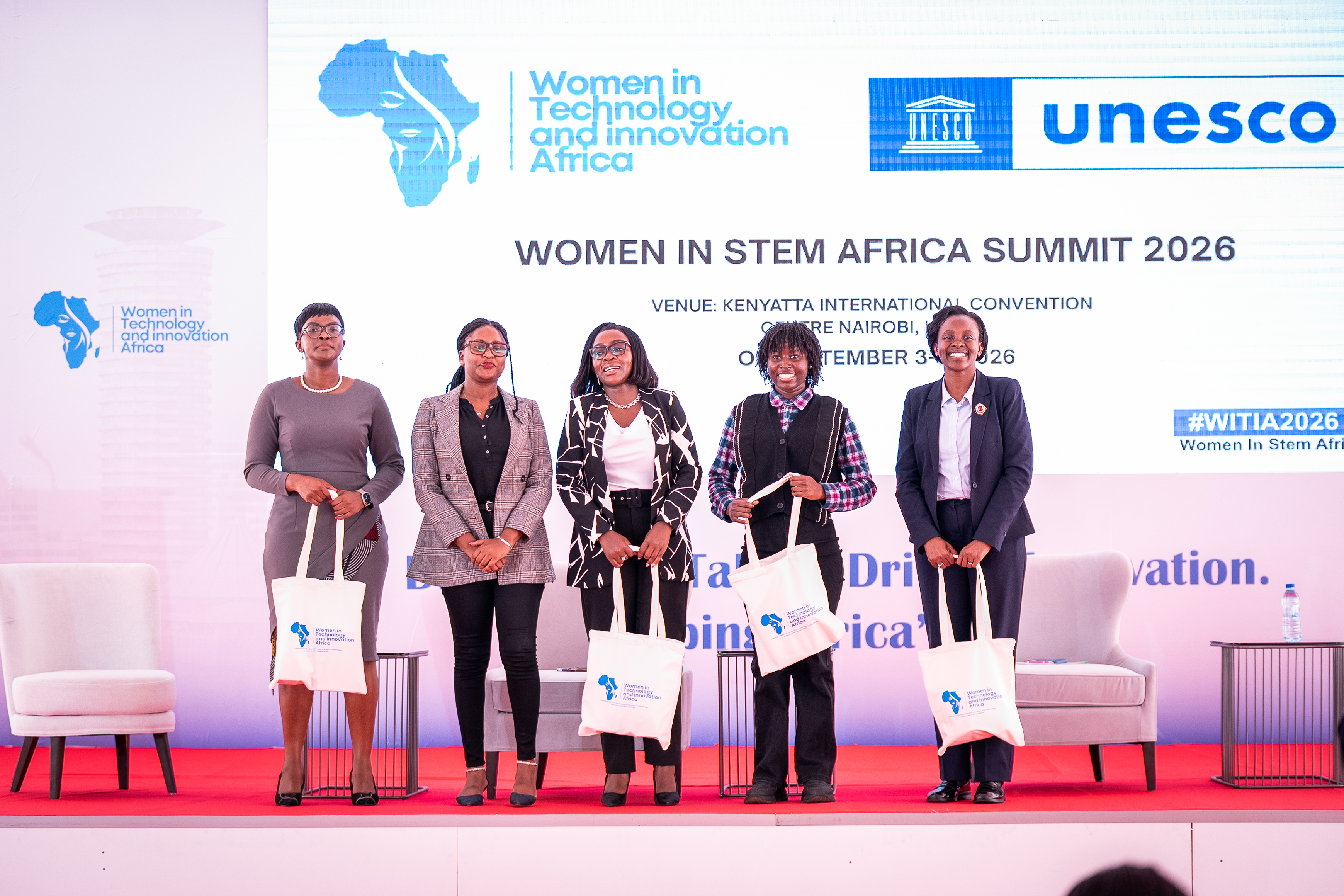 Women standing on stage holding WITIA tote bags