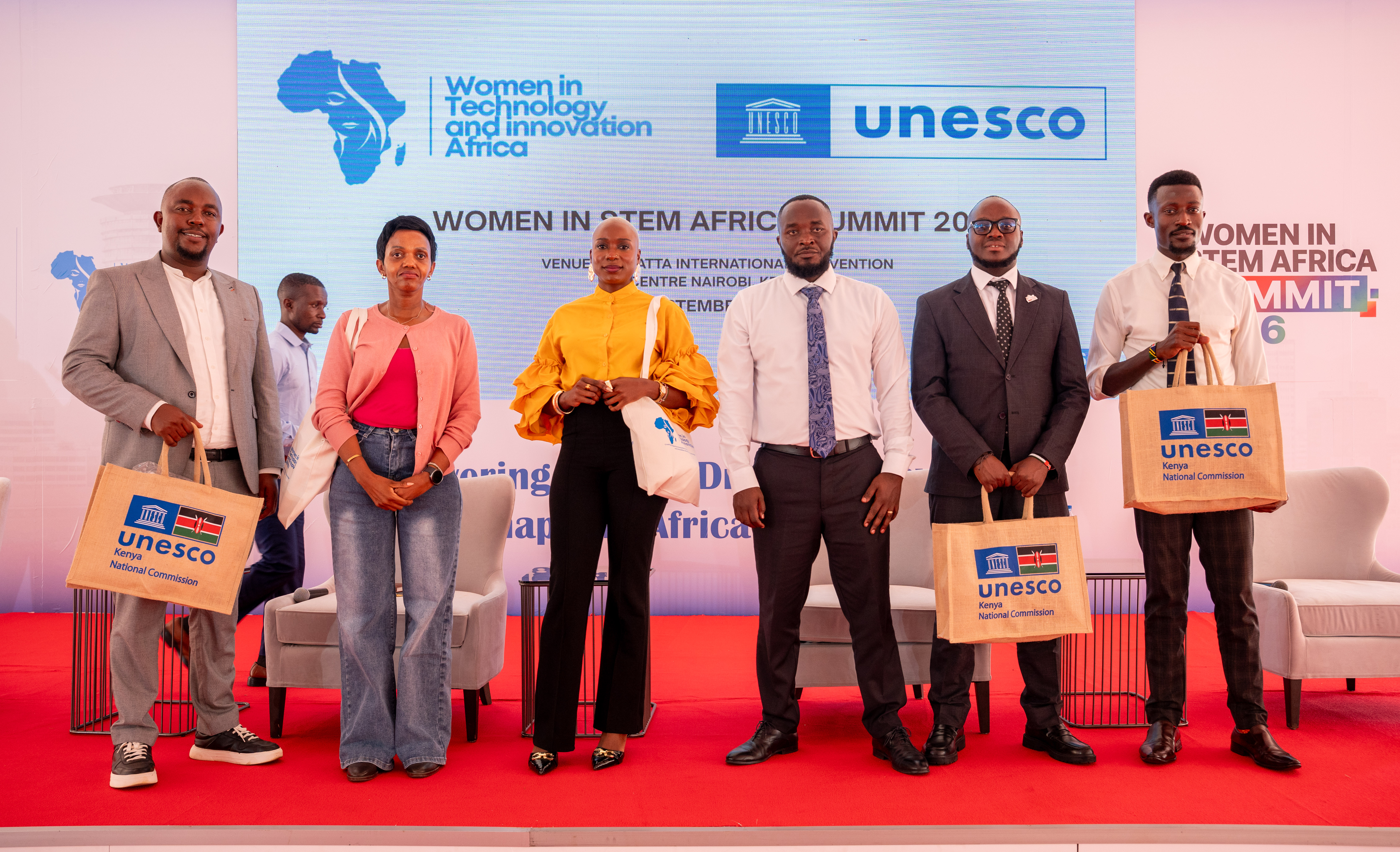 Speakers on stage holding UNESCO gift bags